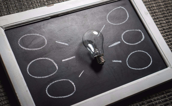 Lightbulb on a chalkboard with idea bubbles drawn branching off from it