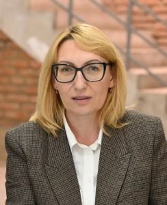 Photo of Natalia Petrenko who has light skin and shoulder-length blonde hair and is wearing glasses and a suit jacket.