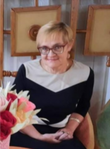 Photo of Tetiana Svatula who has light skin, short blonde hair, and is wearing glasses and a black dress with a white collar.